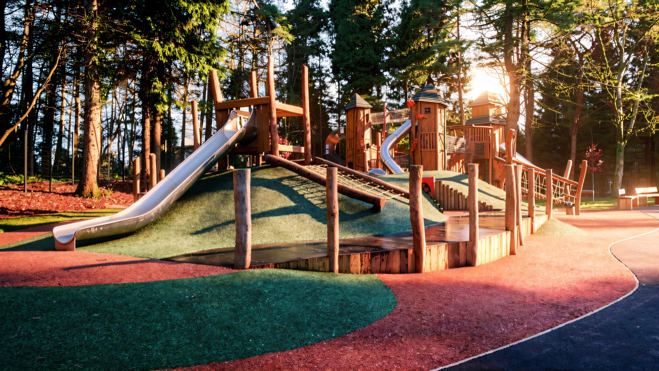 Two long slides set into a green grass embankment on red surfacing at Hillsborough Forest play park