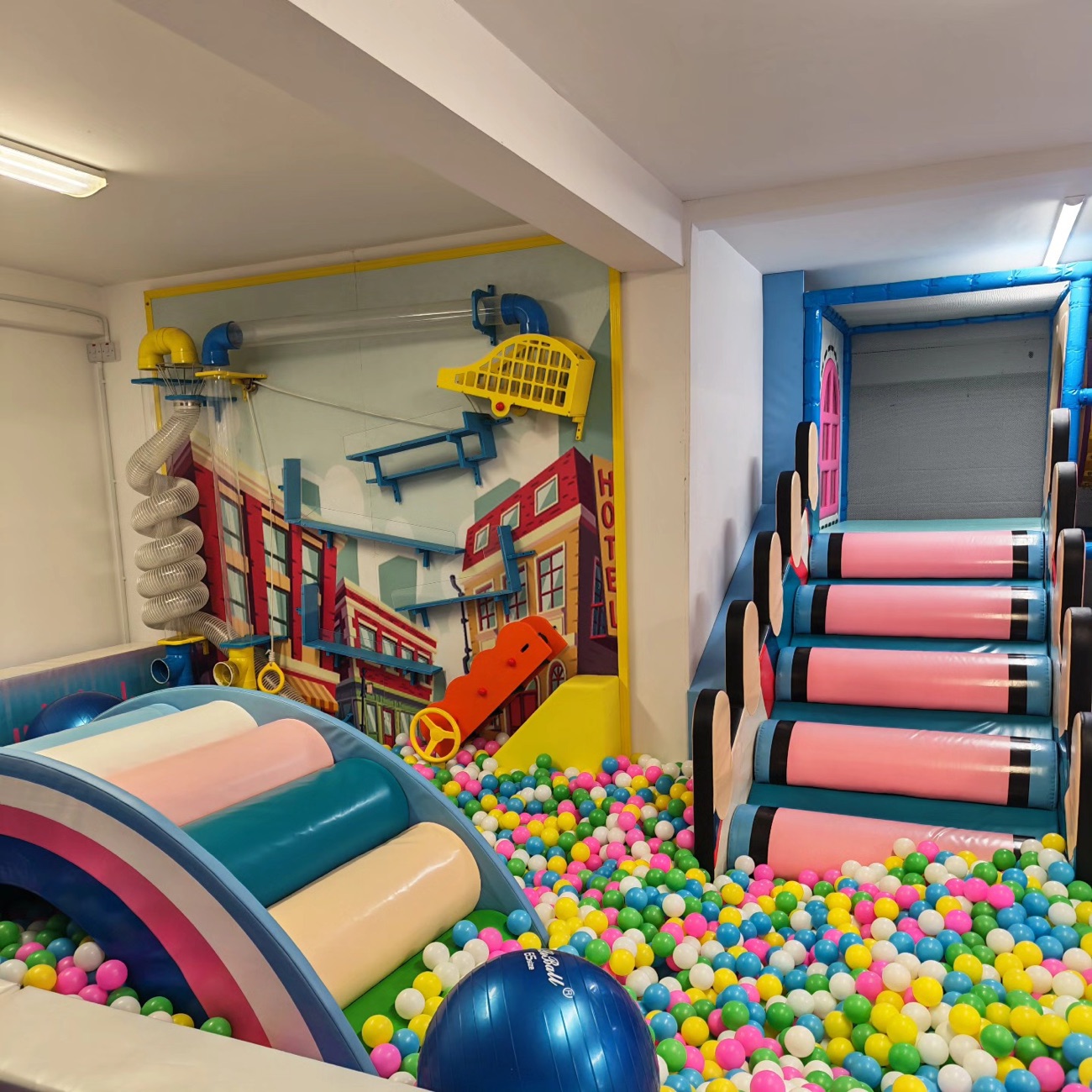 A ball pit and town-themed soft play area at Honeybees Playtown, with a colourful street-scene mural and pink padded steps