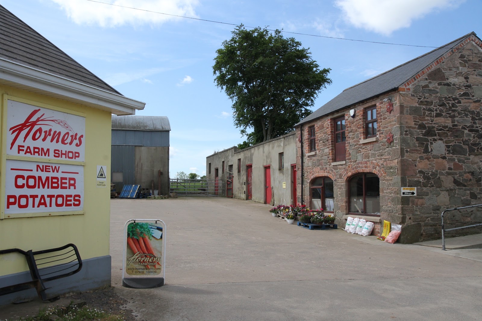 The Horner's Farm Shop sign reading 'New Comber Potatoes' on the yellow gable, with the stone farm buildings behind