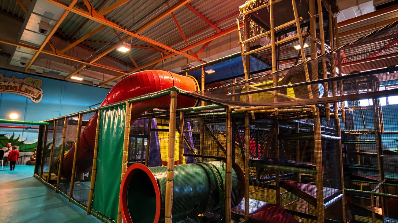 A wider view of the Indiana Land multi-level play frame with a red tube slide and a green padded crawl tunnel