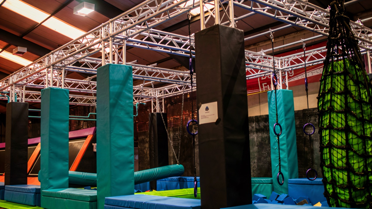 The ninja obstacle course — teal and black padded towers, hanging rings and a green cargo net over foam pits