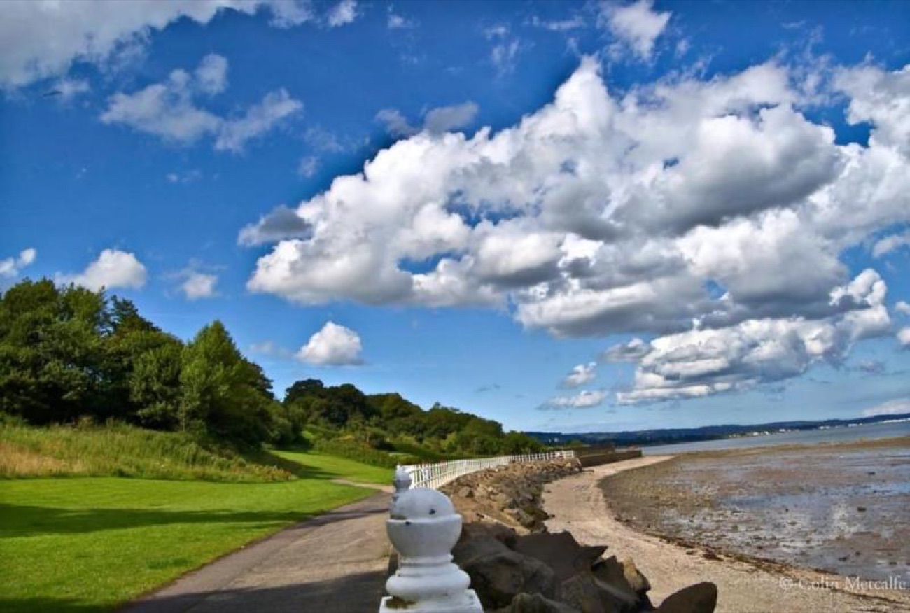 The shore path at Jordanstown with a shingle beach on one side and big clouds overhead