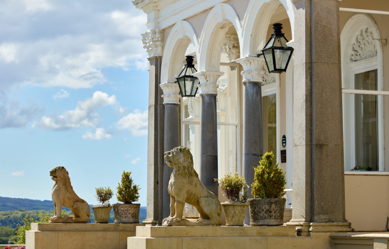 The arched stone colonnade at the entrance to the manor, flanked by carved stone lions and potted bay trees