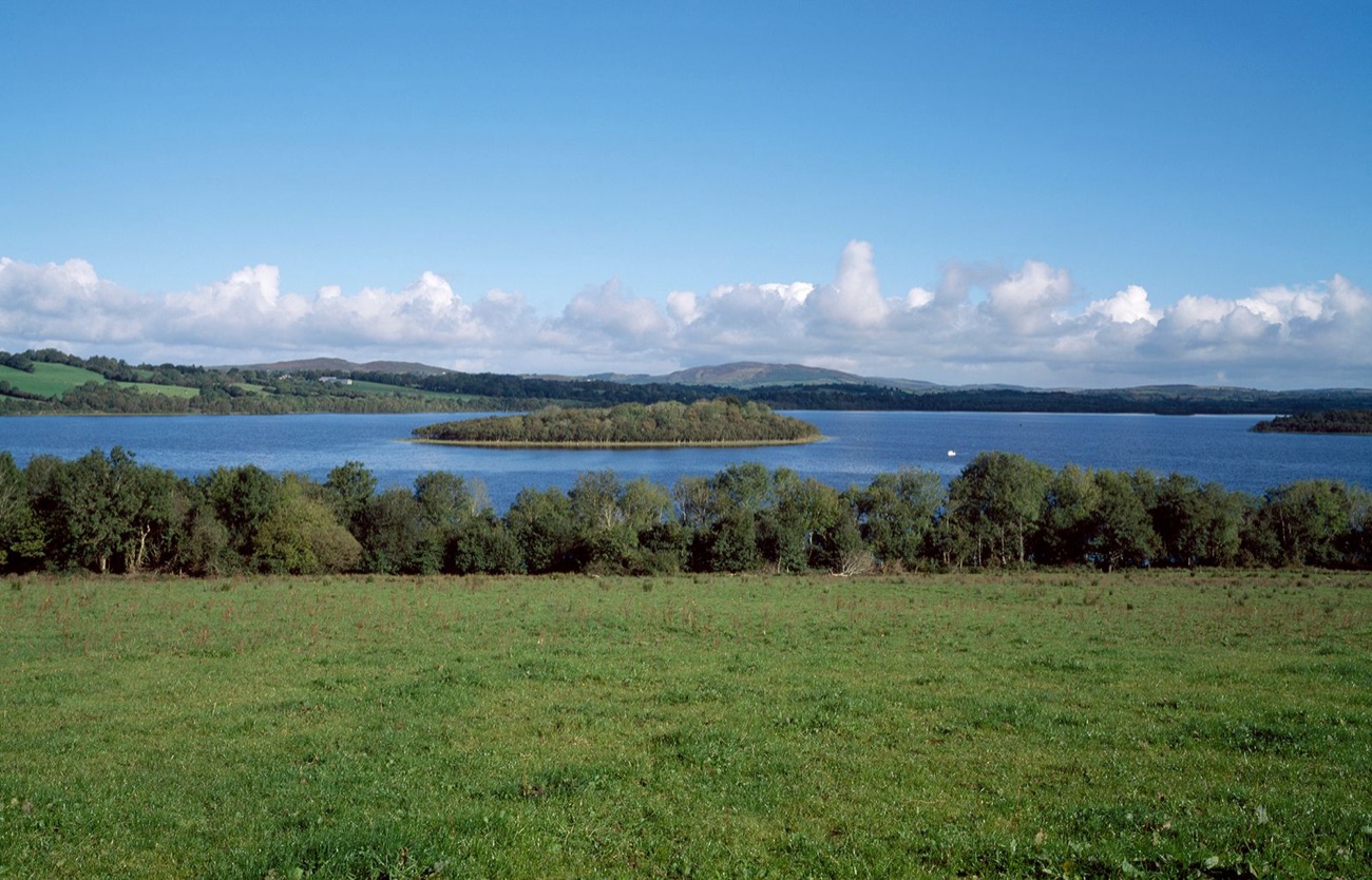 A calm stretch of Lower Lough Erne with a wooded island and low green hills beyond