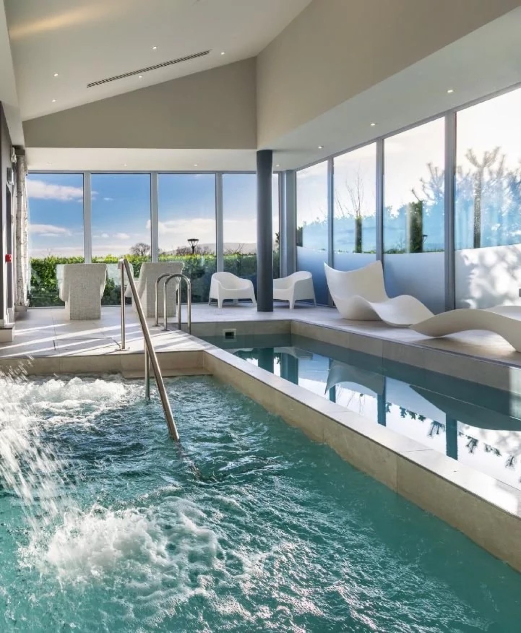 The vitality pool with its water jets and loungers, tall windows opening onto the green countryside.