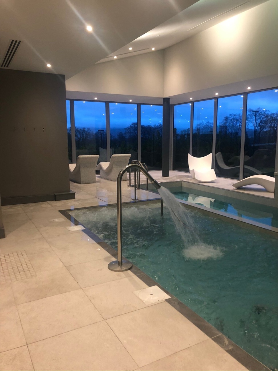The same pool room at dusk, the sky turning blue beyond the glass wall.