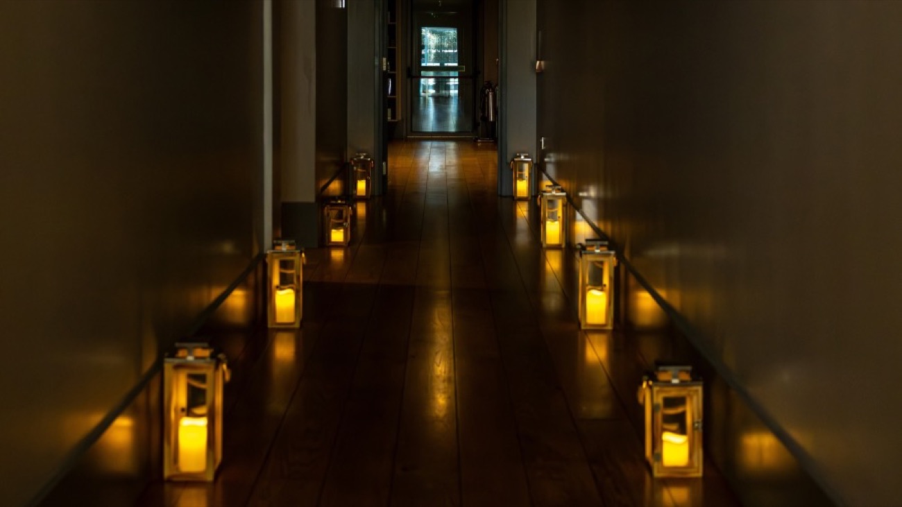 A hushed treatment corridor lit by a row of candle lanterns on a dark timber floor.