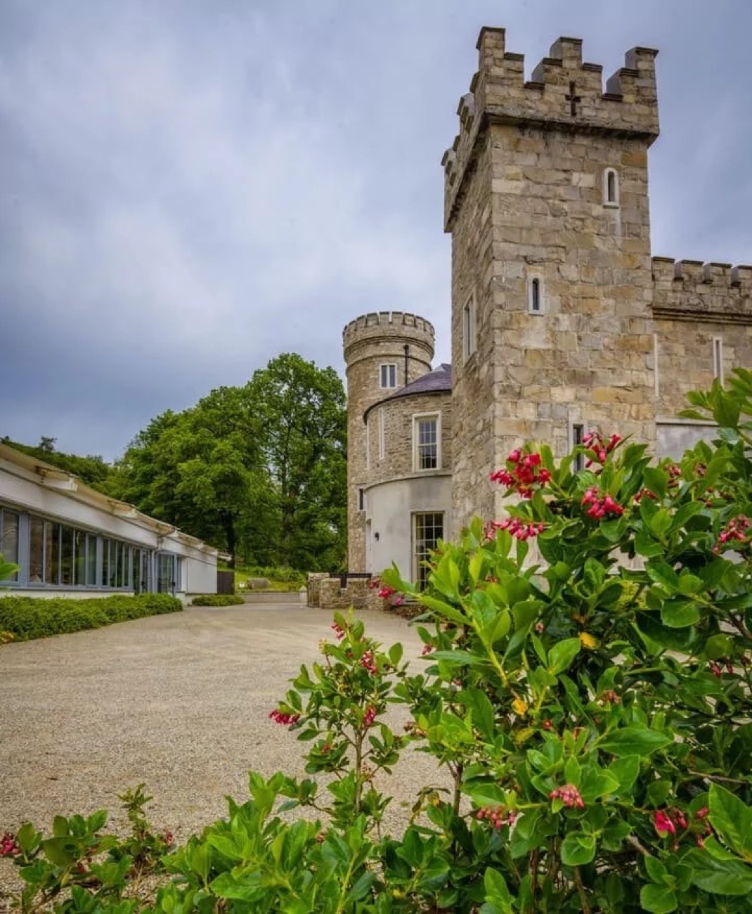 The Gothic castle's battlemented stone tower, the low spa building beside it and flowering shrubs in front.