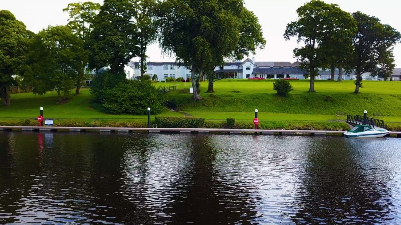 The hotel seen from across Lough Erne, with the marina jetty and a moored boat on the calm water