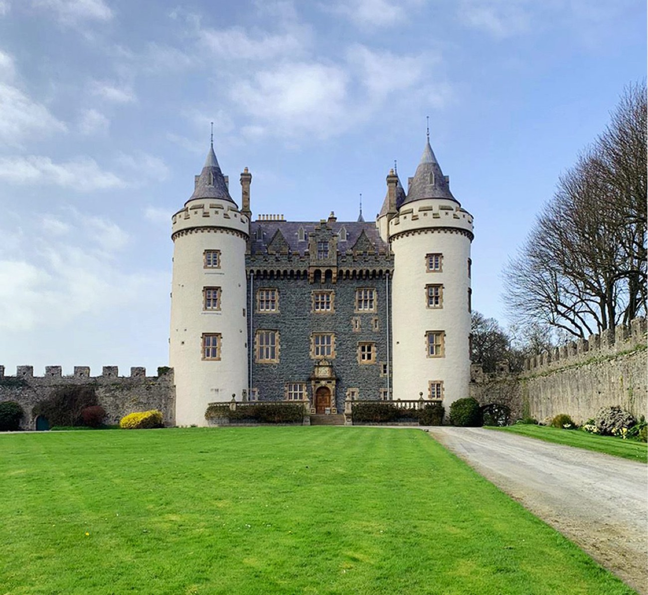 The front of Killyleagh Castle from the lawn, two round white towers with grey conical roofs flanking the house