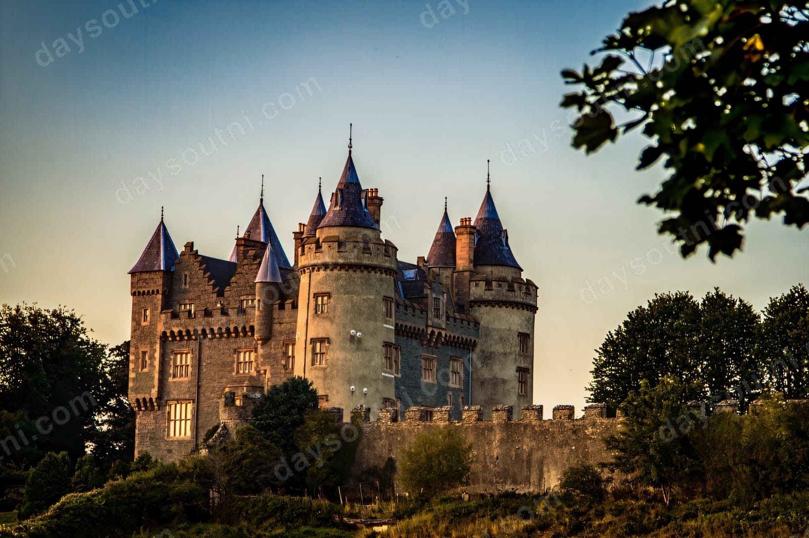 The turrets and blue-coned towers of Killyleagh Castle rising above the trees at golden hour