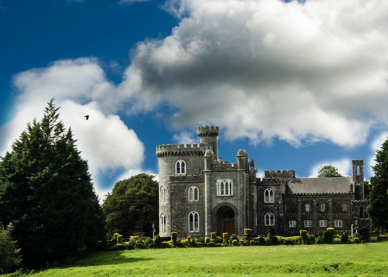 Killymoon Castle seen from the front under a big sky, its round tower and battlements rising above the parkland trees