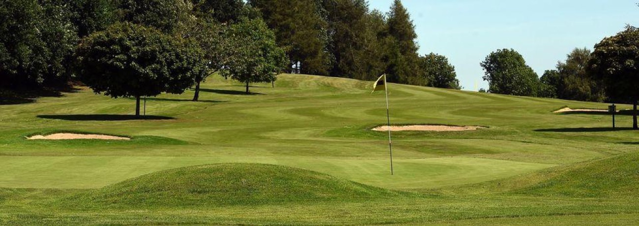 A green and flag on the parkland golf course at Killymoon, with mown fairways, bunkers and mature trees