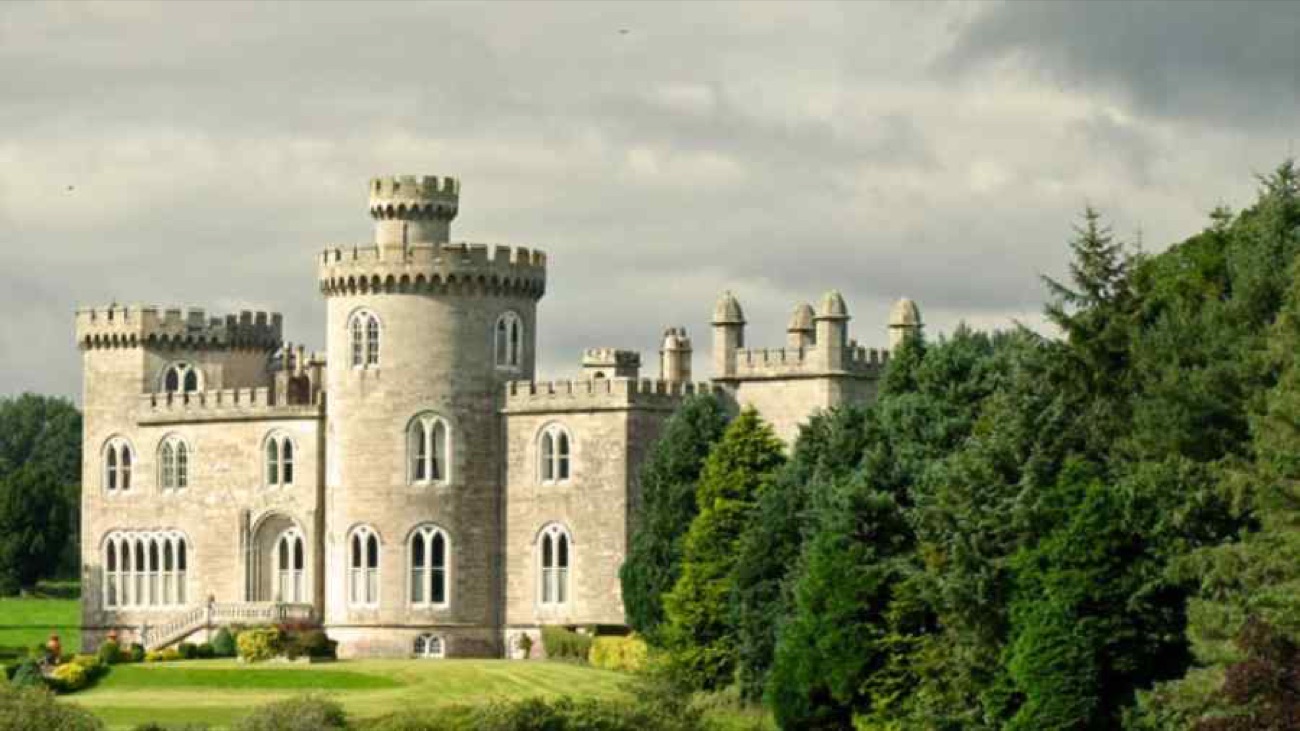 Close view of Killymoon Castle's battlemented round tower and turrets in pale stone against a cloudy sky