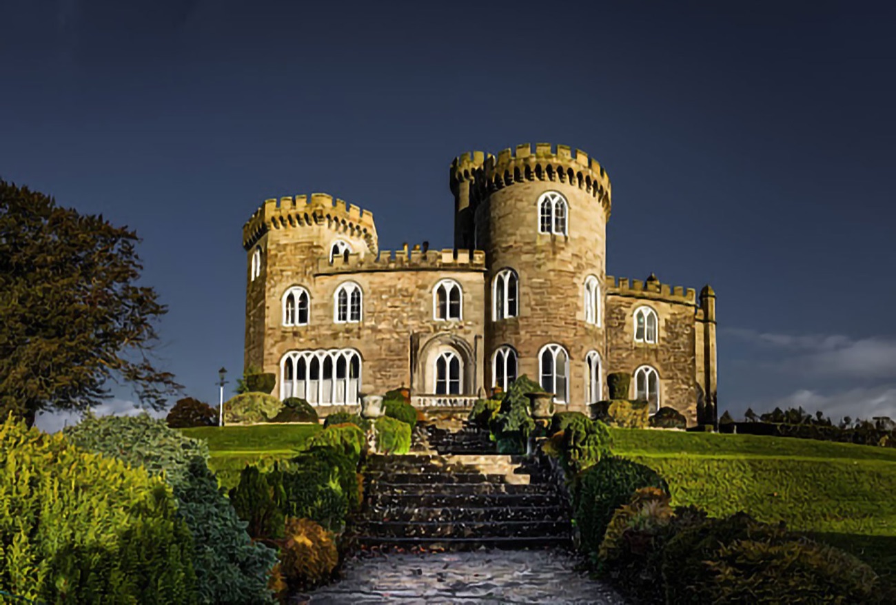 Killymoon Castle lit against a dark evening sky, showing its round towers and gothic windows
