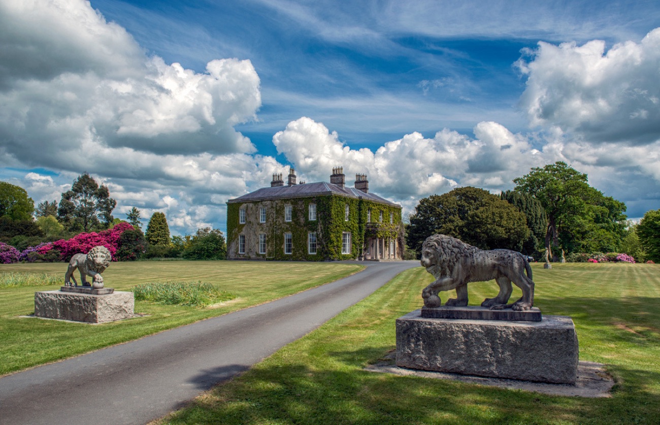 The Georgian house across green parkland, flanked by stone lion statues