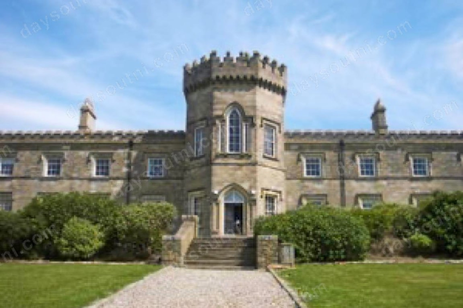 Learmount Castle in sunshine — a Gothic-revival stone house with a battlemented central tower, seen across a clipped lawn