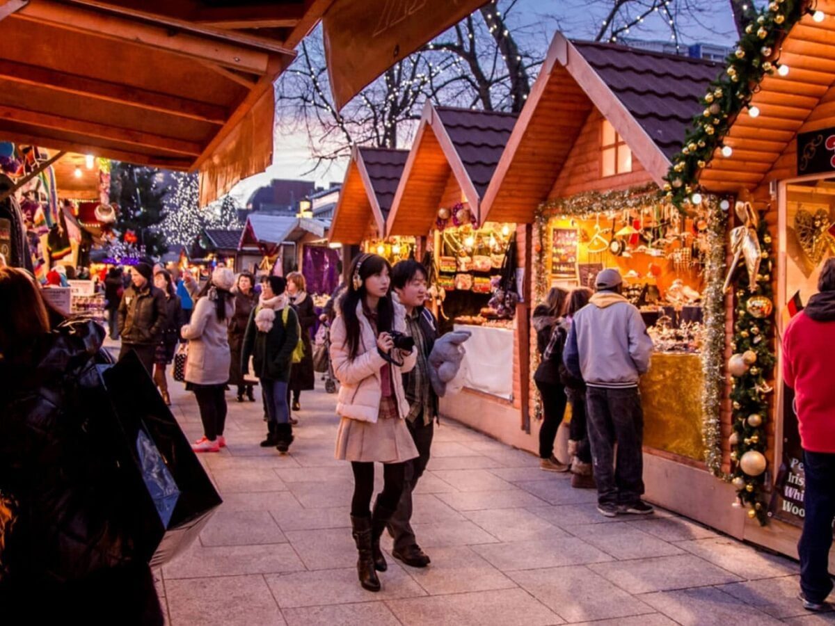 Families walking past festive food stalls and warm lights at an evening Christmas market