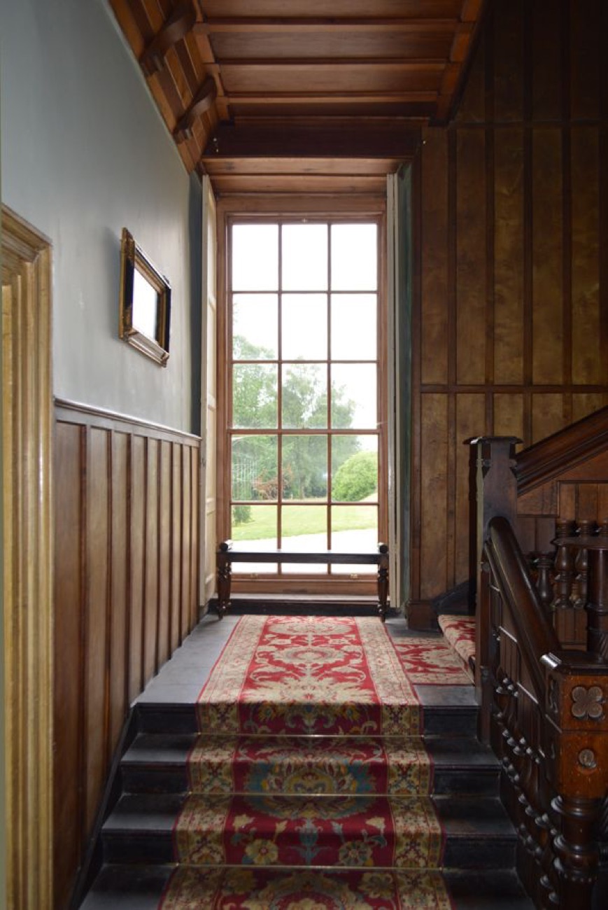 A dark oak-panelled staircase landing inside Lissan House, with a patterned red runner and a tall window looking out to the grounds