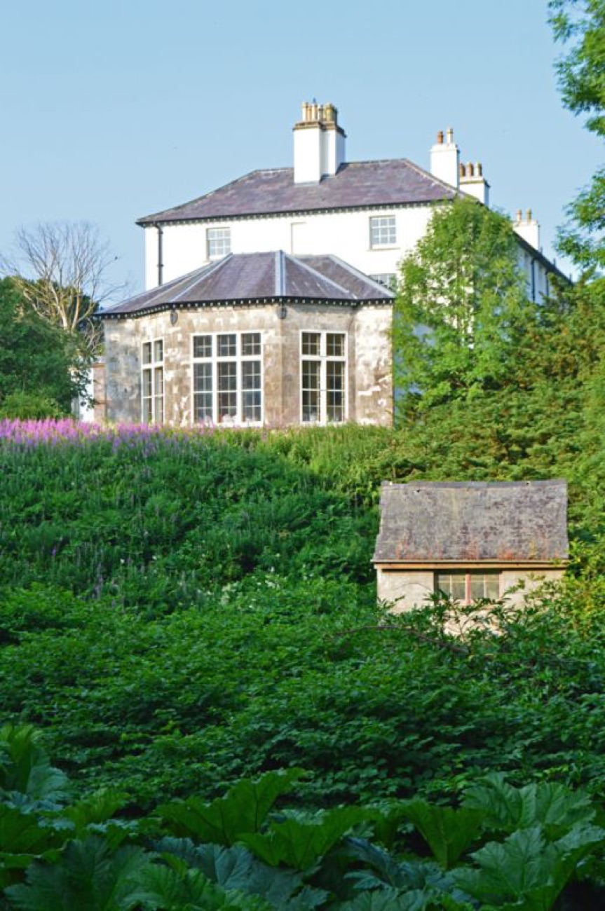 The stone bow wing of Lissan House rising above a lush garden of tall flower spikes and giant leaves, with a small stone garden building
