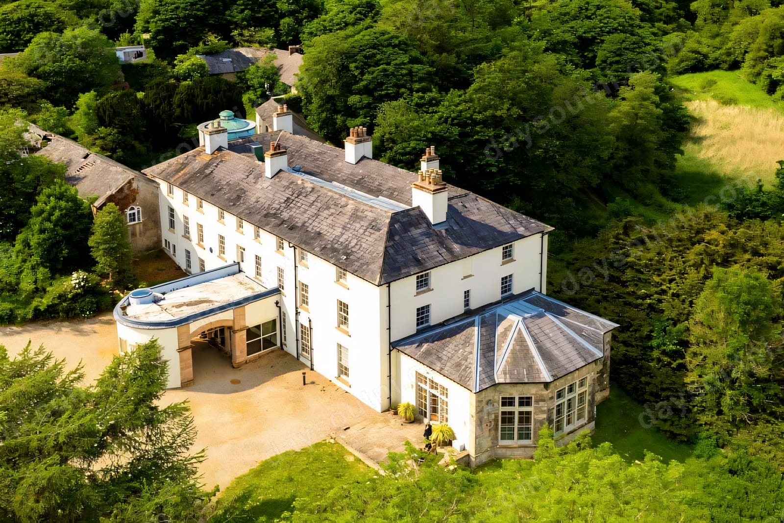 An aerial view of the white rambling manor of Lissan House set among green woodland, with its stone bow-window wing