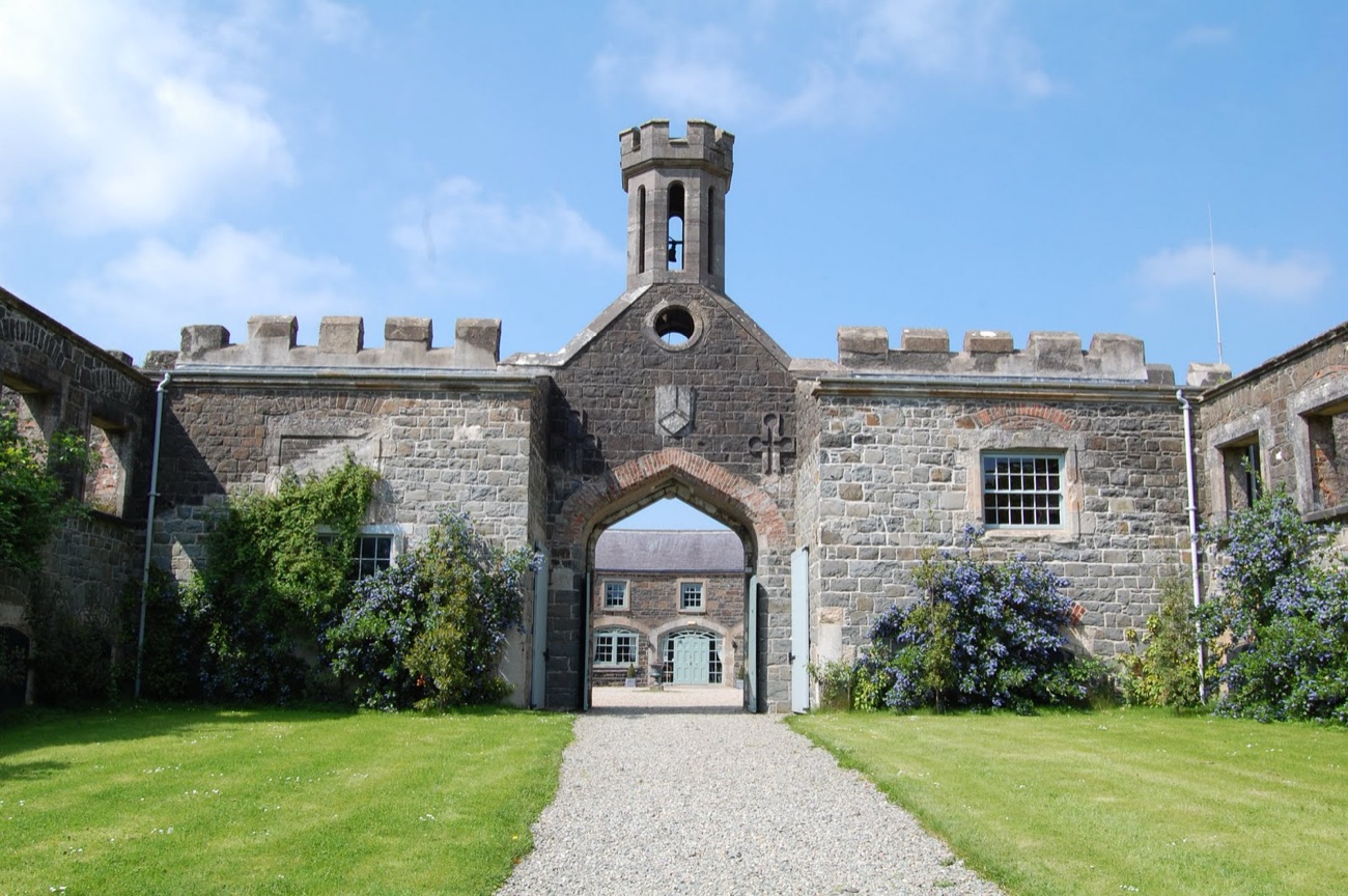 The castle courtyard front — a stone archway under the clock tower, framed by flowers