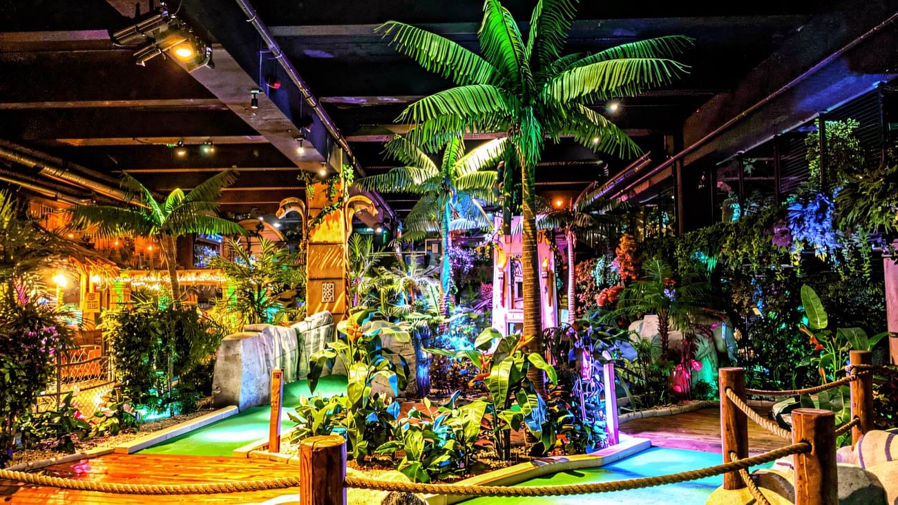 Tropical palms and greenery arching over the lit fairways of the indoor course