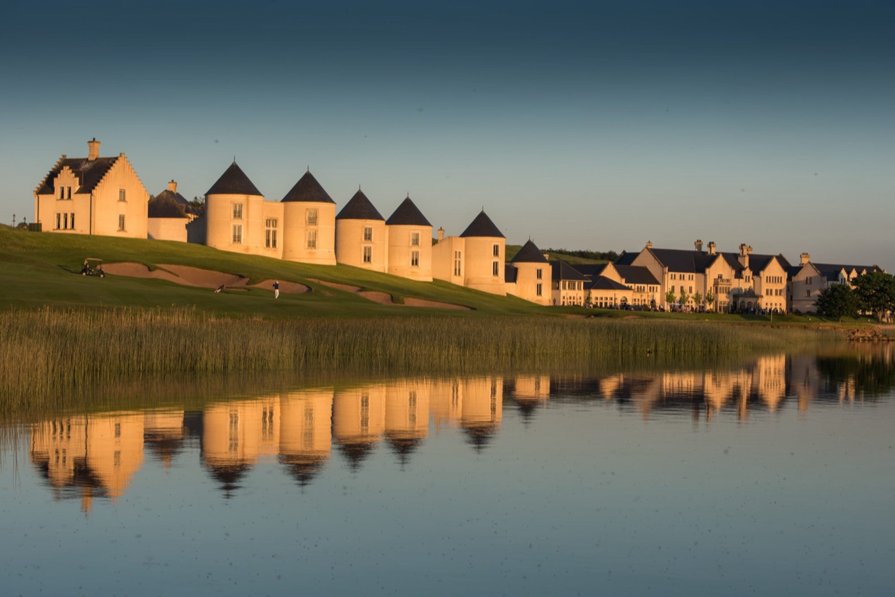 The resort's turrets glow gold at sunset, mirrored in the still lough.