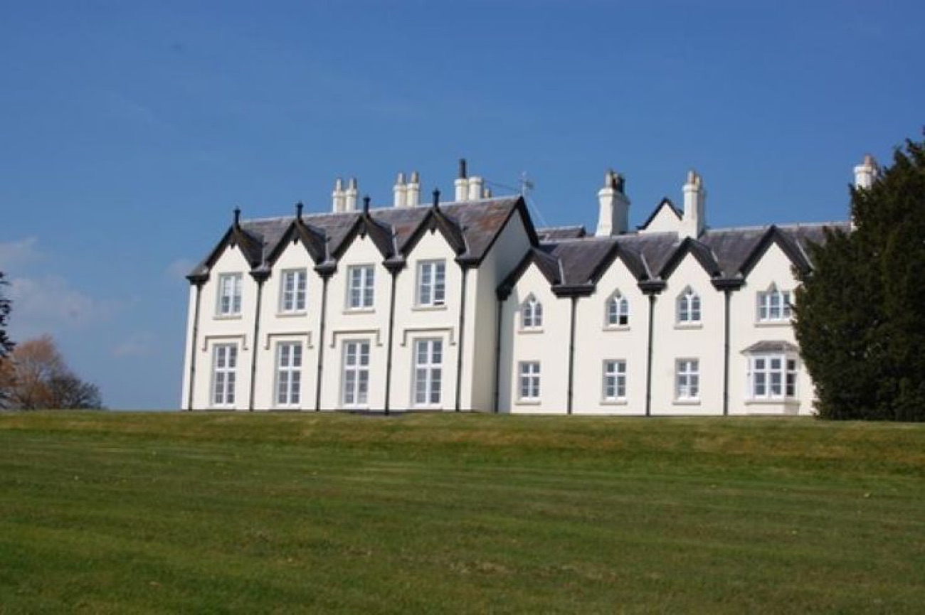 The full front elevation of Loughgall Manor across a broad lawn in spring sunshine