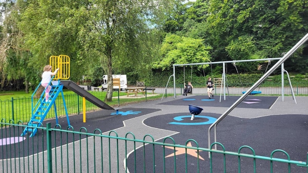The play park at Lover's Retreat with bright blue and yellow equipment set in the trees