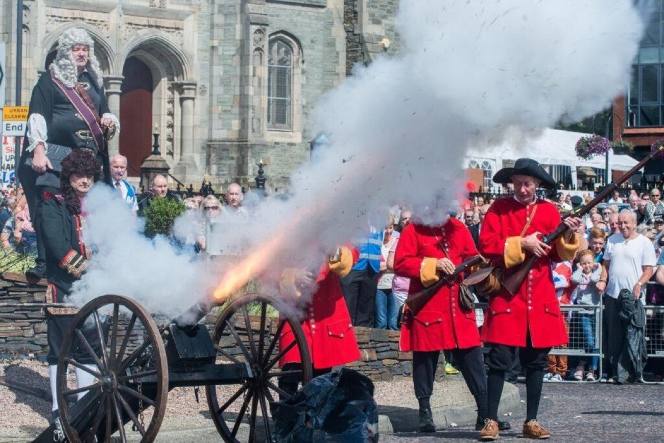 Costumed re-enactors firing a cannon in a Guns of the Siege demonstration at the Maiden City Festival, watched by a crowd