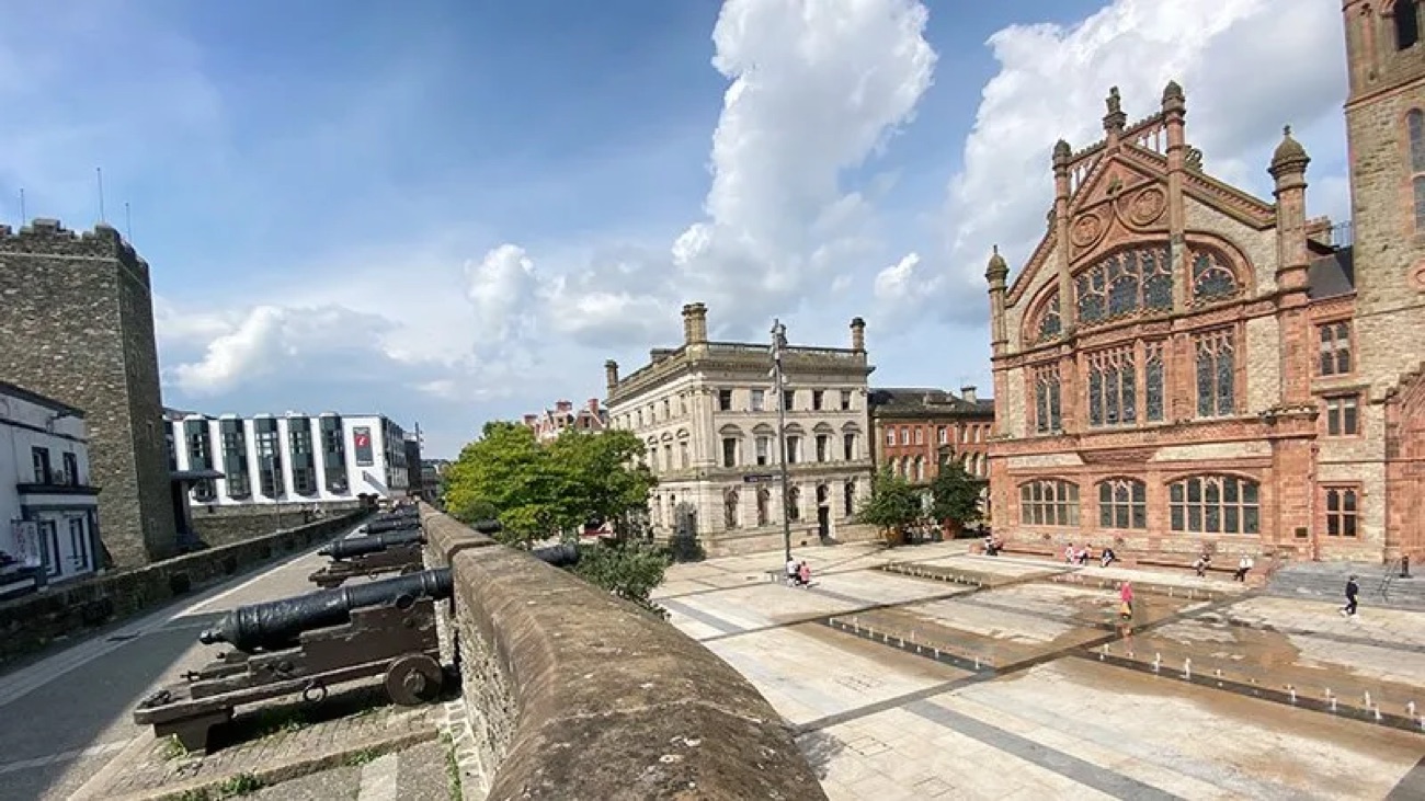 Derry's city walls lined with old cannons, with the historic Memorial Hall beyond