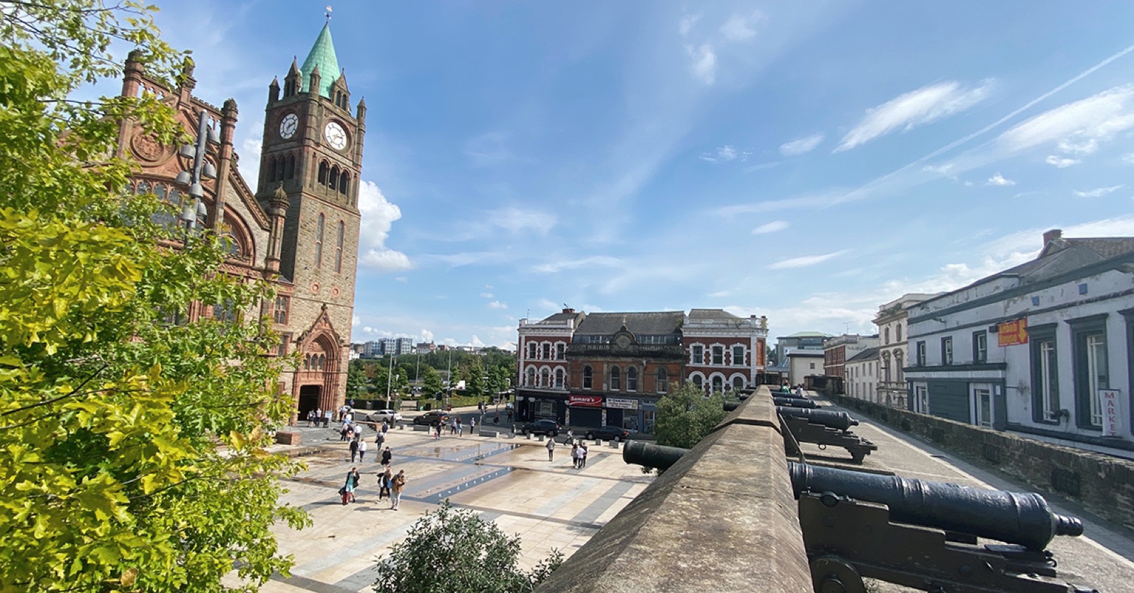 The Guildhall clock tower and the historic cannons on Derry's 17th-century city walls under a blue sky