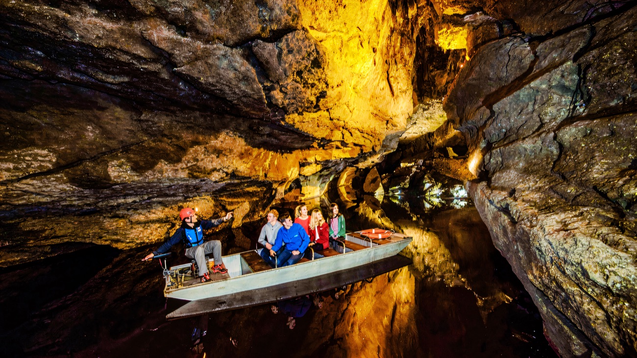A small boat gliding along the underground river through a wide lit cavern