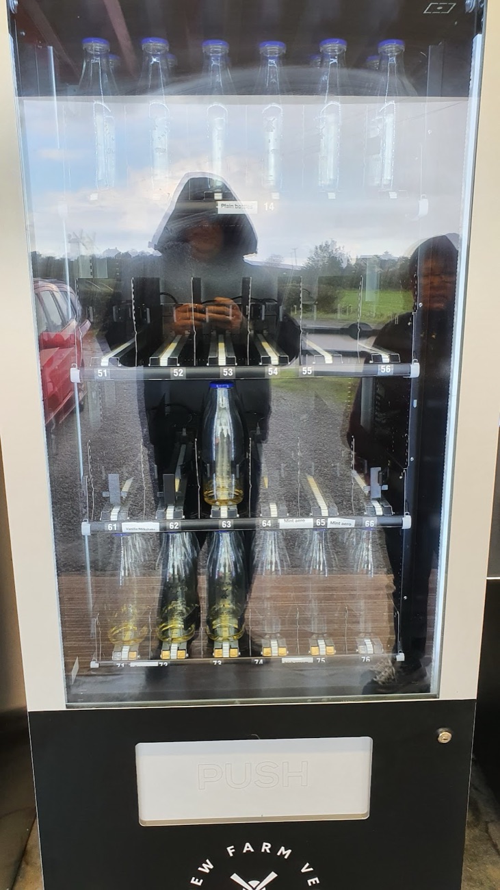 A glass-fronted milk vending machine stocked with bottles inside the shed