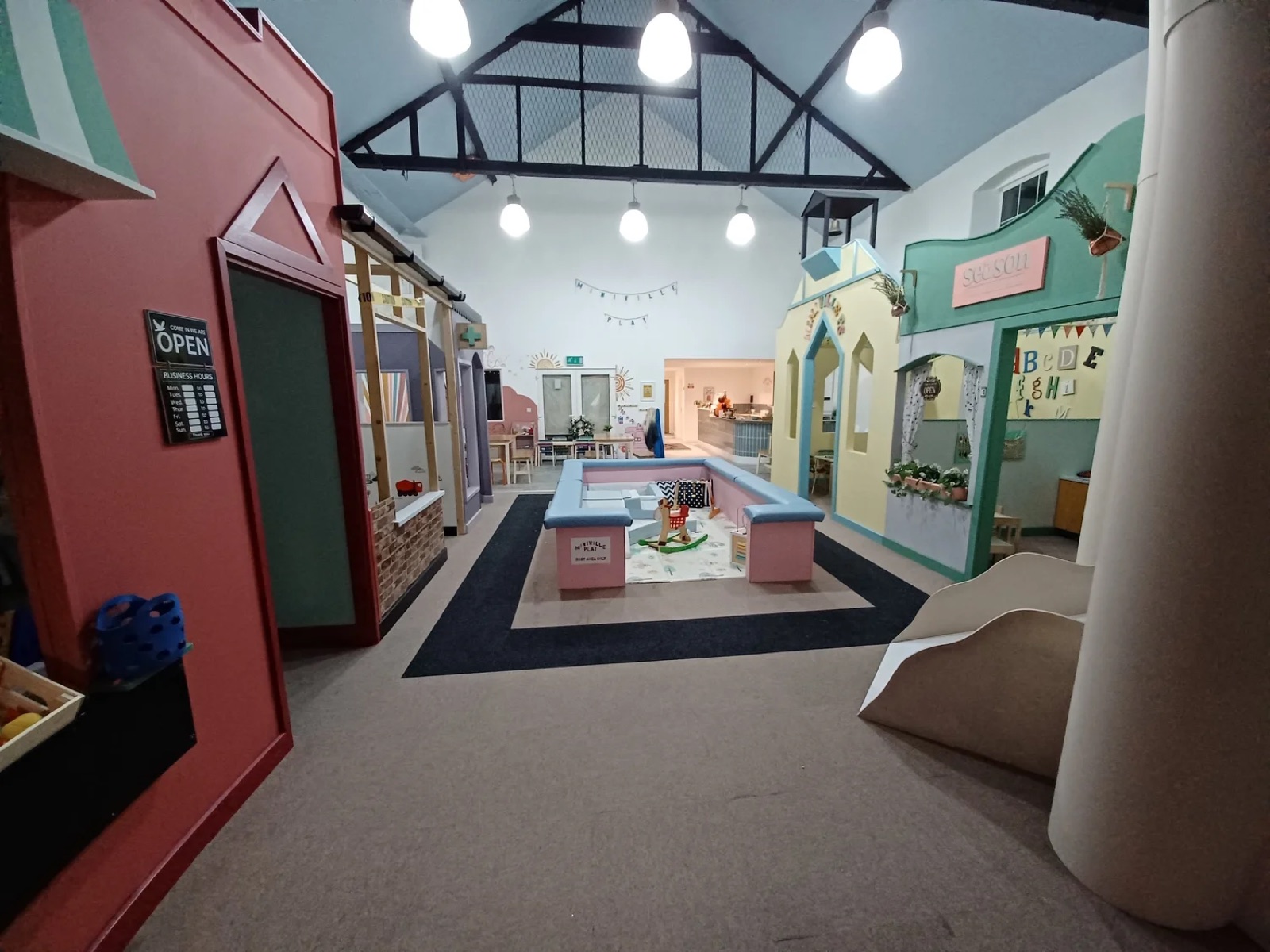 The indoor mini-town at Mini Ville Play, Carrickfergus, with pastel pretend shops and houses lining a play street under a vaulted roof