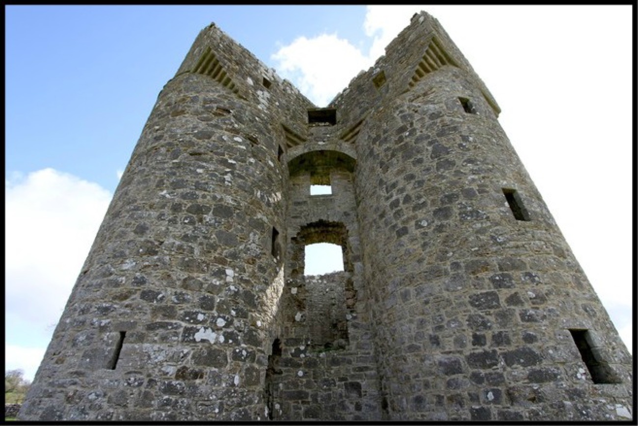 Looking up between Monea Castle's twin towers at the corbelled crow-stepped turrets against the sky