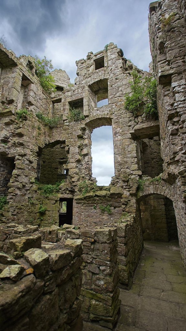 Inside the roofless shell of Monea Castle, tiers of empty window openings against a moody sky