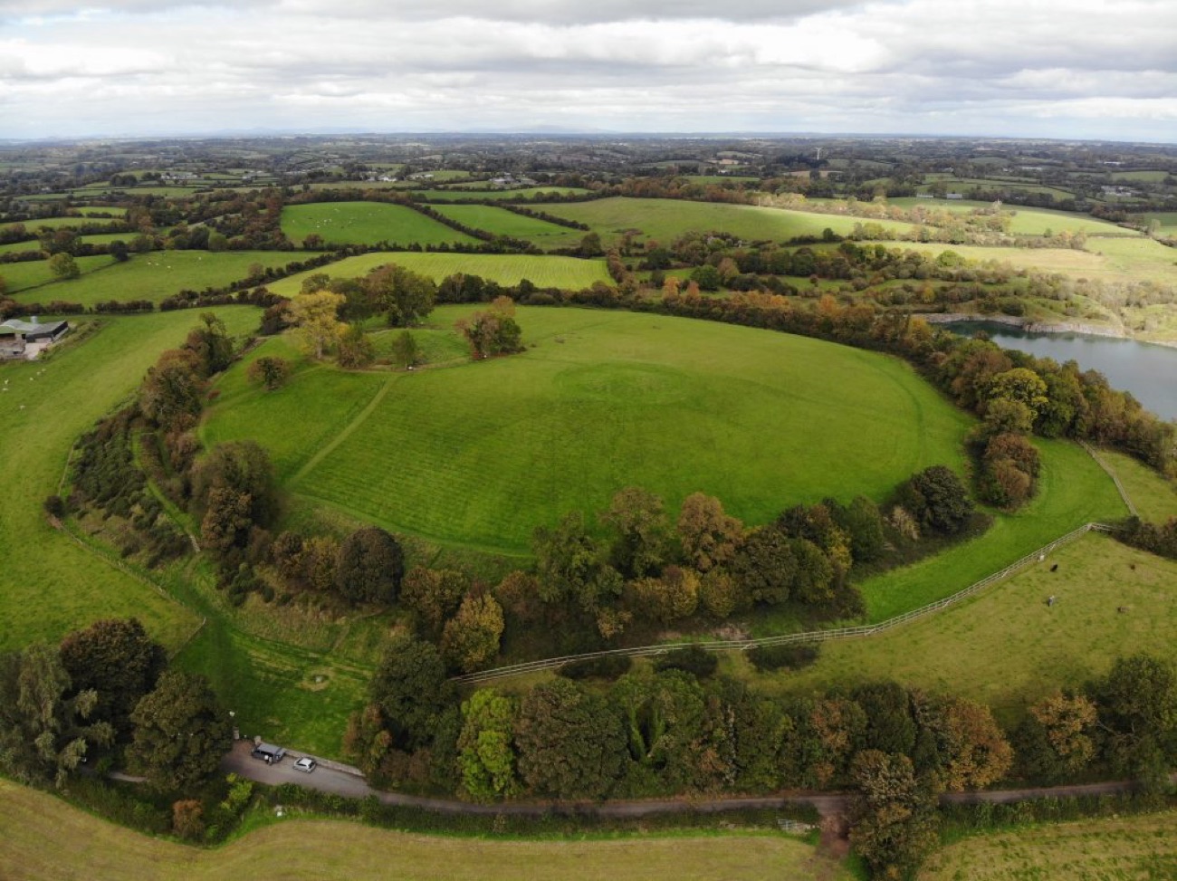 Autumn aerial of the whole Navan Fort enclosure with a quarry lake in the distance