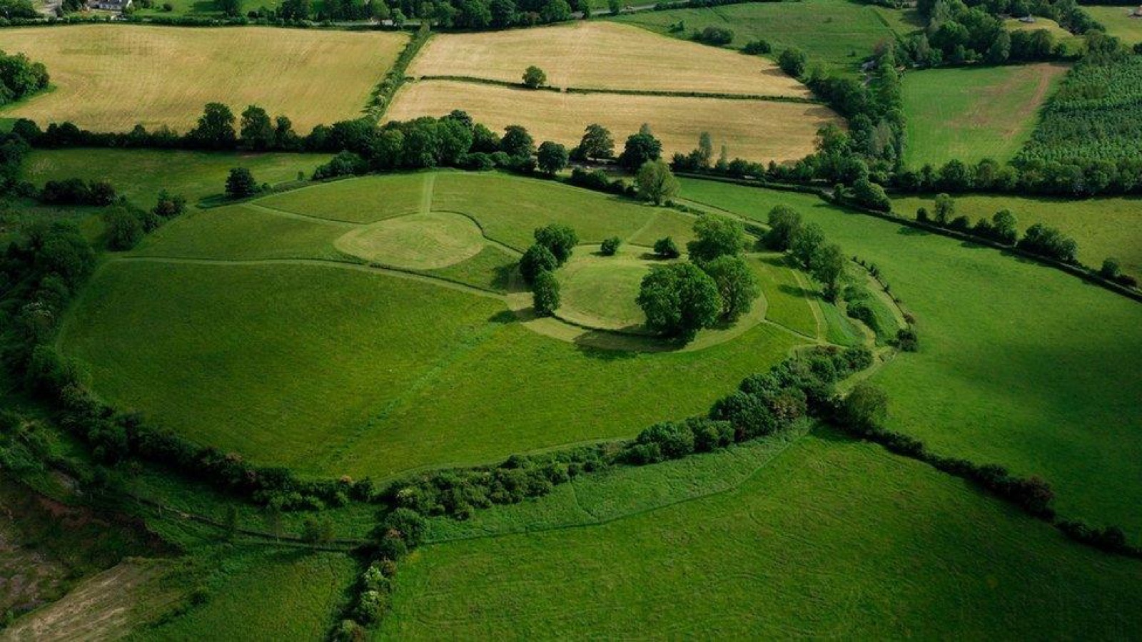 Aerial view of the great circular earthwork of Navan Fort, its central grassy mound ringed by a bank and ditch, surrounded by farmland