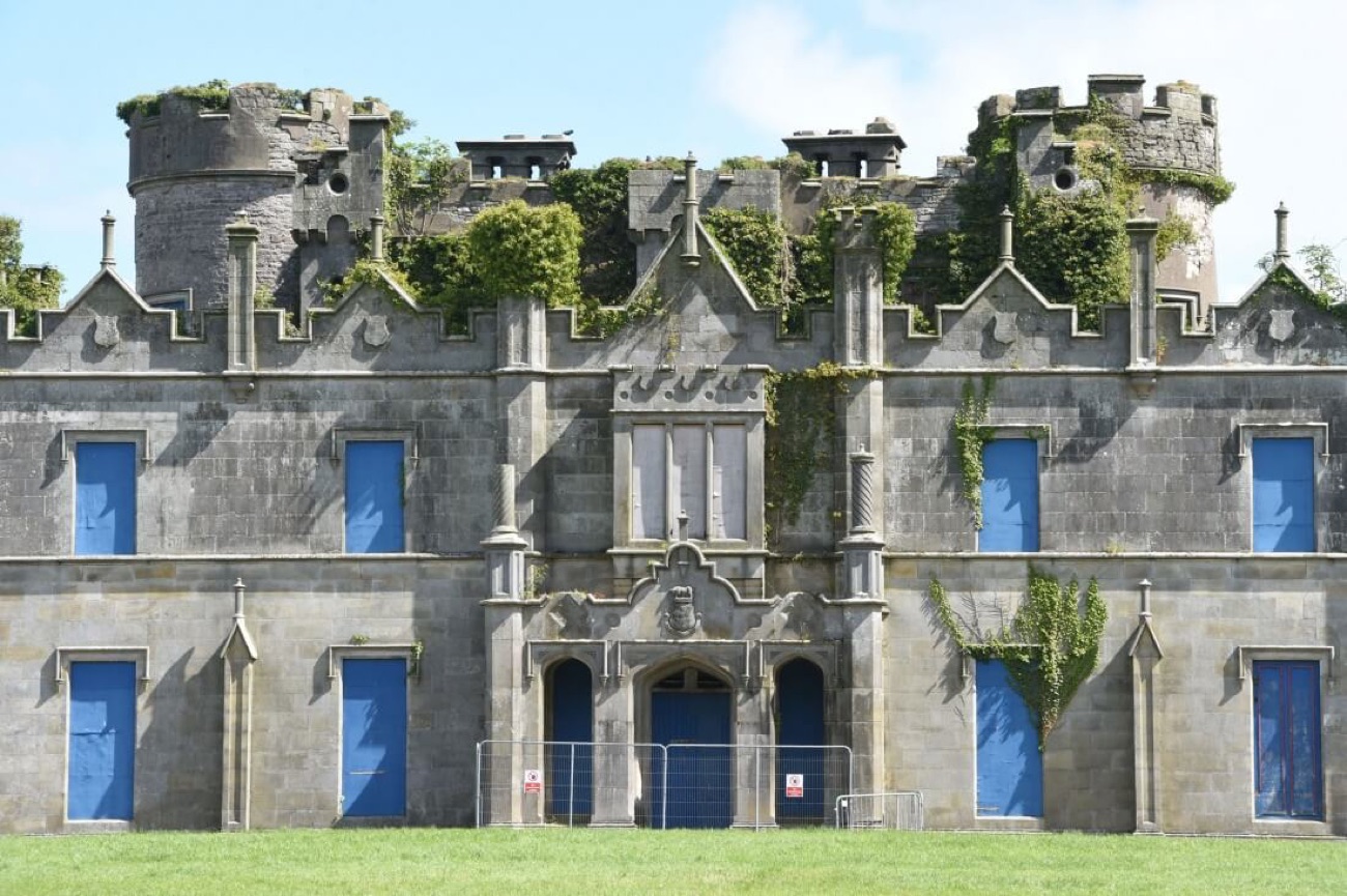 Close-up of Necarne Castle's derelict facade, ivy over the battlements, boarded-up windows and a metal safety fence across the front doors