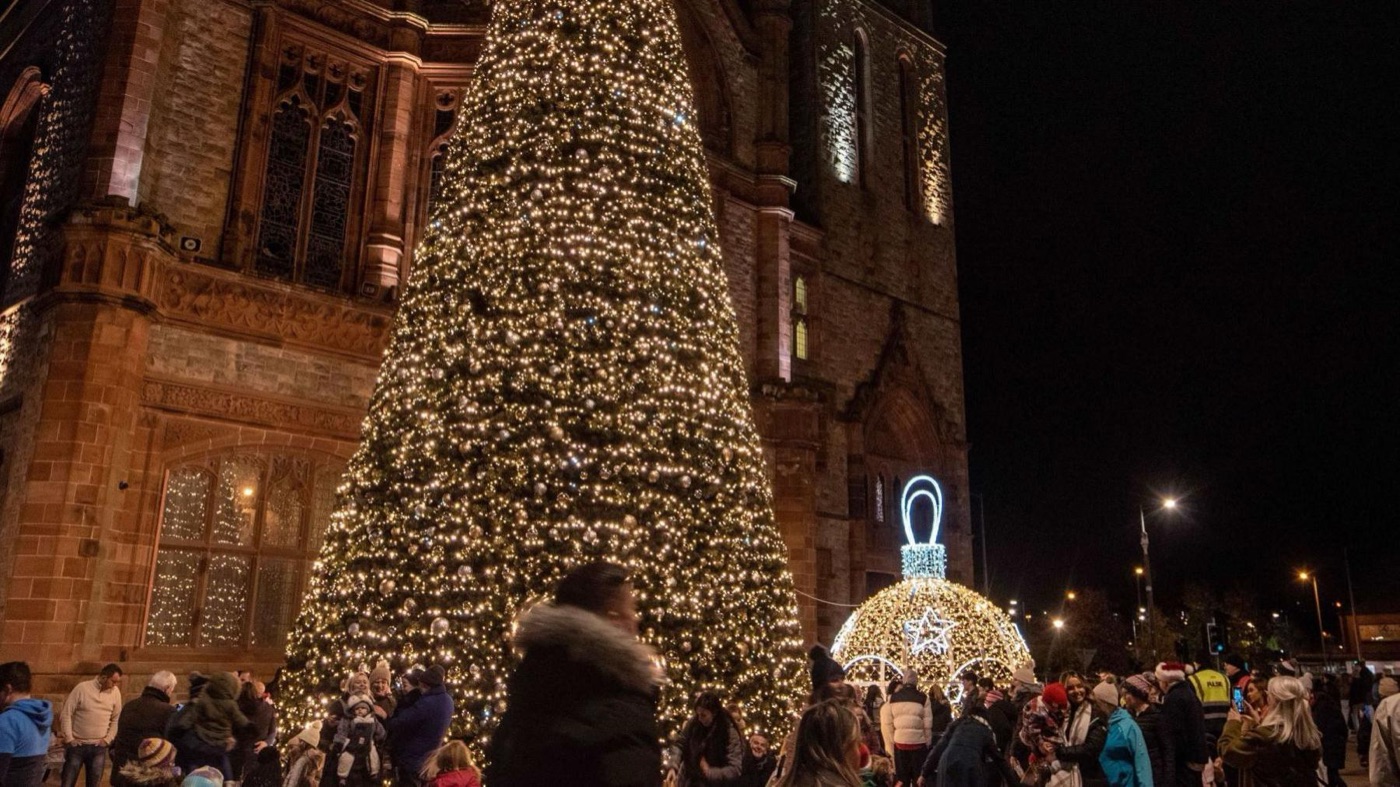 A town centre Christmas tree lit at night with a crowd gathered around it