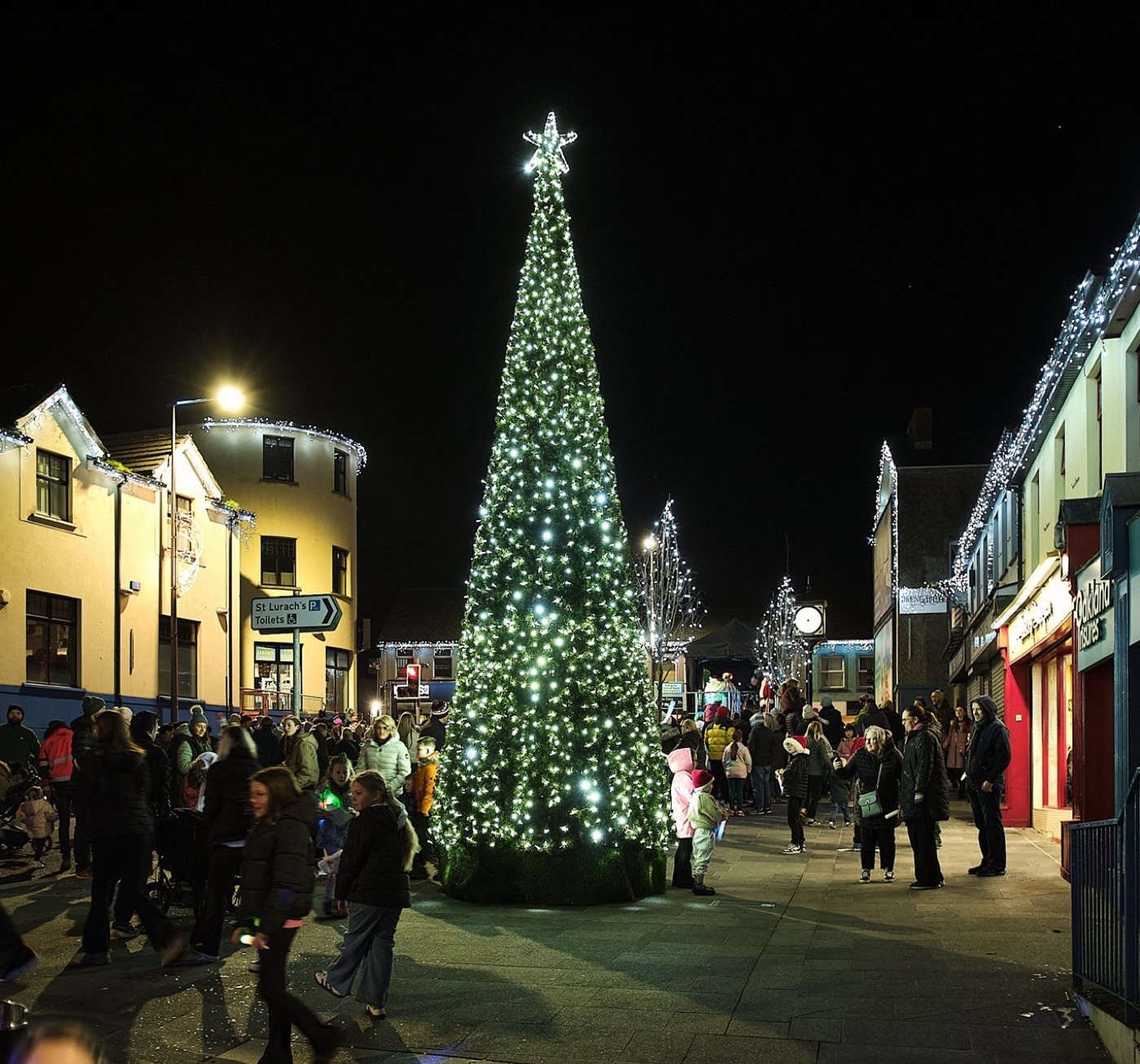 A small town Christmas tree lit at night with people gathered on the street