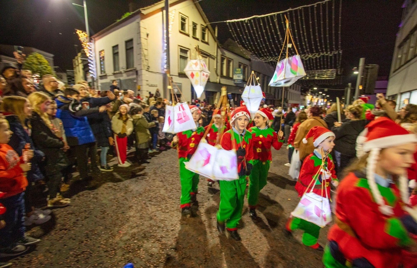 Children in elf costumes parading with lanterns at a Christmas lights switch-on