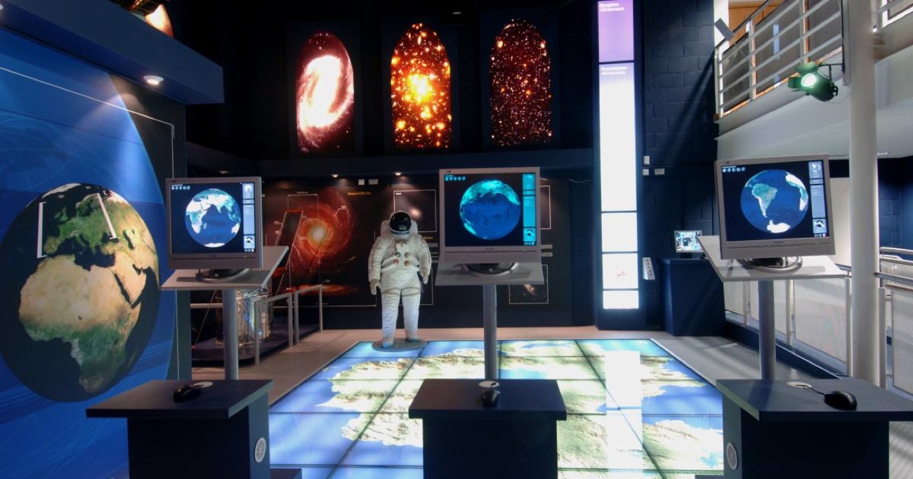 A space science gallery with an astronaut suit, an interactive world-map floor and galaxy images