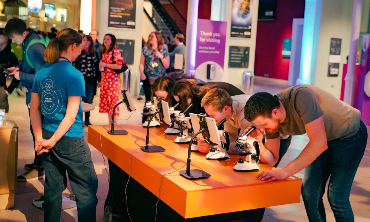 Visitors looking through a row of microscopes at a hands-on science exhibit
