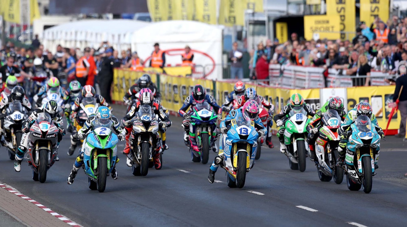 A pack of road-racing motorbikes launching off the start line at the North West 200 with grandstands behind