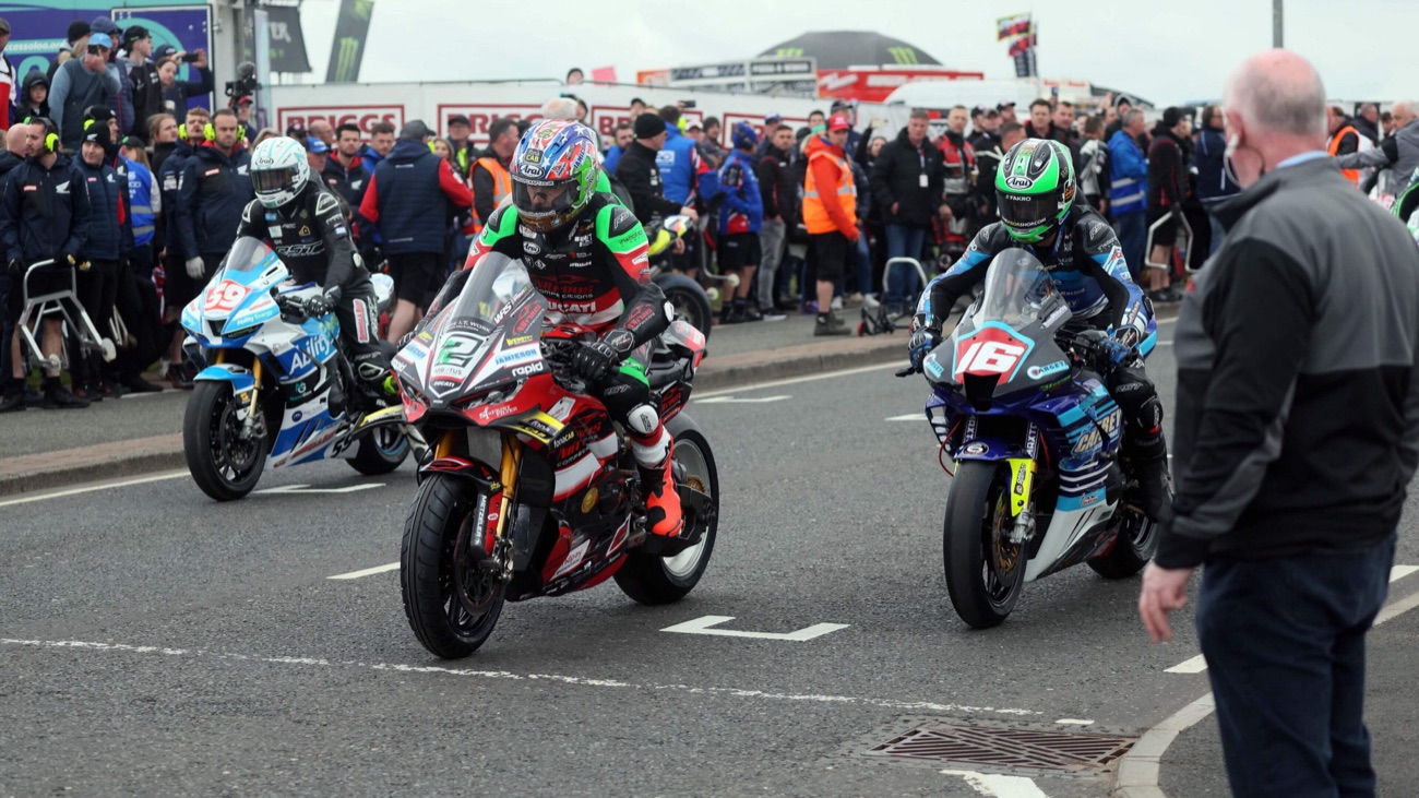Riders and race bikes in the paddock with fans looking on at the North West 200