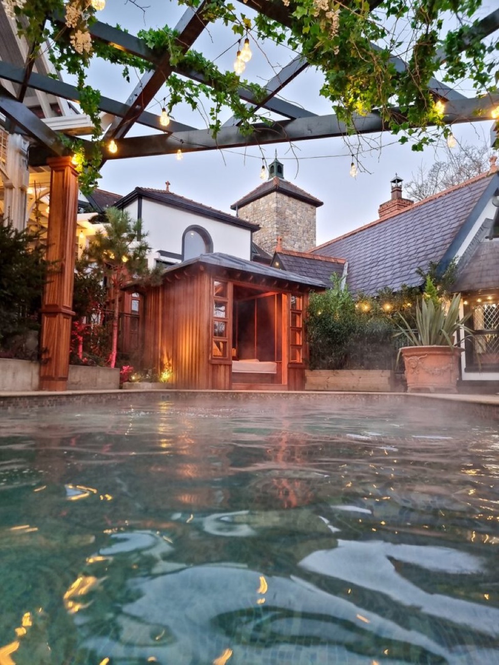 The outdoor pool at dusk, festoon lights strung above and the inn's old chimney behind.