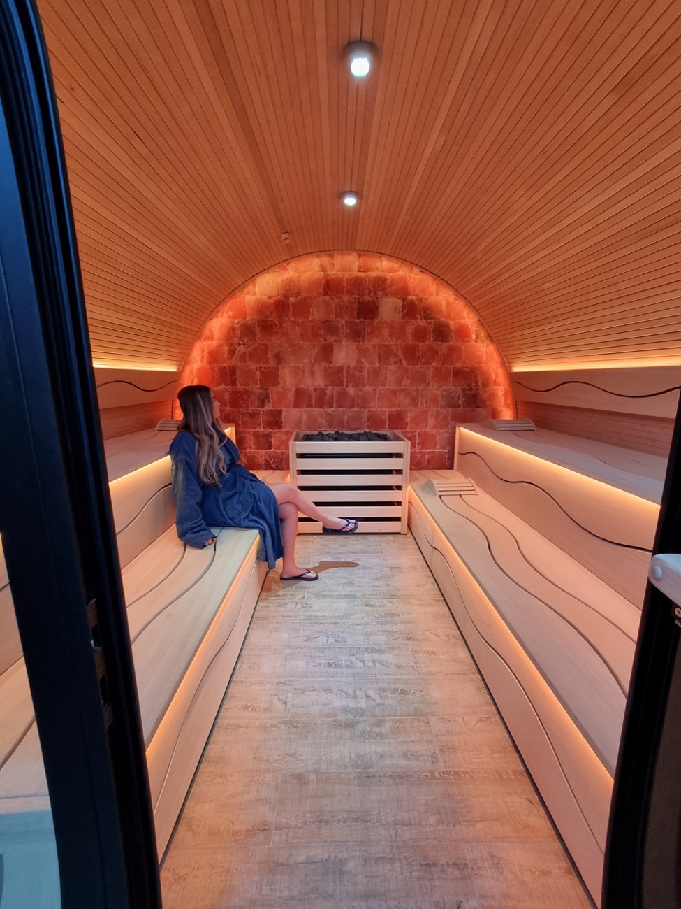The salt sauna: a curved cedar cabin with a glowing Himalayan salt-brick wall.